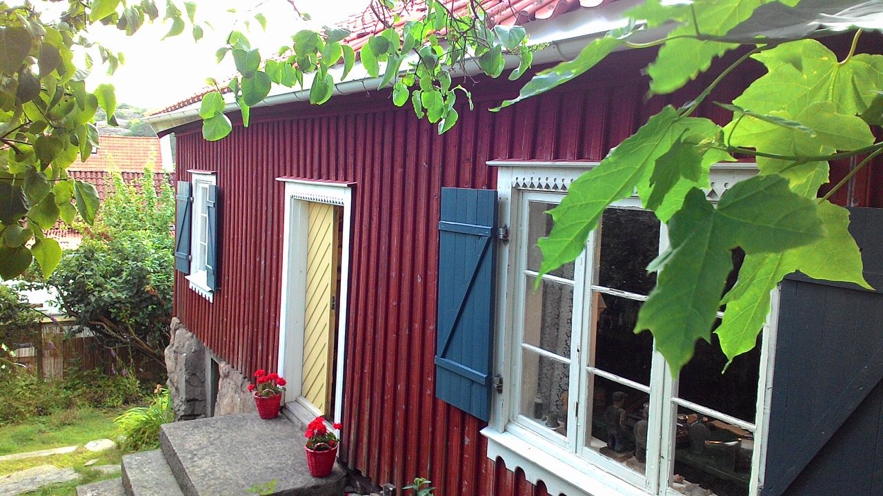 Bockehuset i Grebbestad ett rött trä­hus med blå fönsterluckor och blommor vid trappen, hem till Kulturföreningen Gamla Grebbestad.